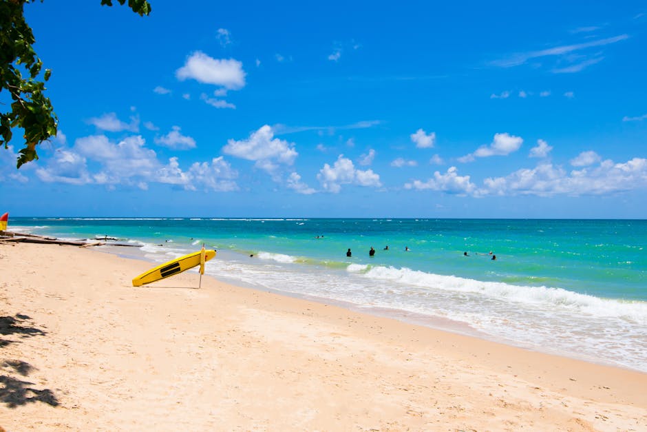 Idyllic tropical beach with turquoise waters, sandy shore, and a yellow surfboard under a bright blue sky